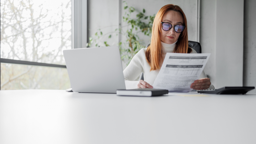 Woman reviewing financial documents at a desk with a laptop, illustrating portfolio review and risk management.