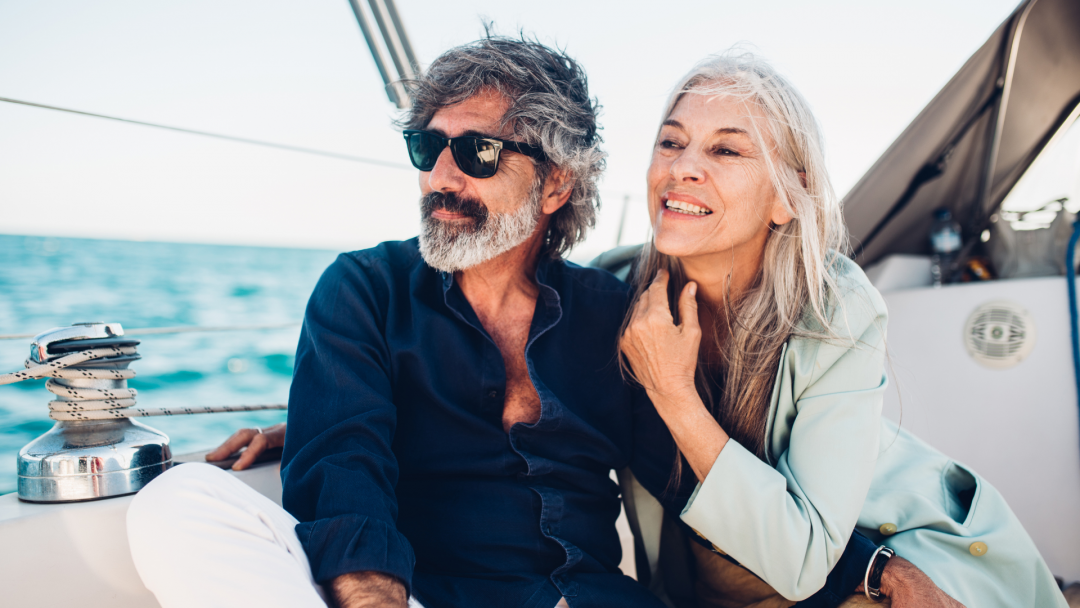 Smiling mature couple on a sailboat, representing financial freedom and flexibility.
