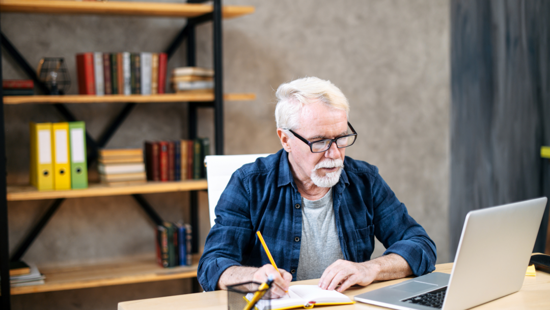 Older man studying finances at a desk with laptop, symbolizing retirement planning and overcoming market fears.