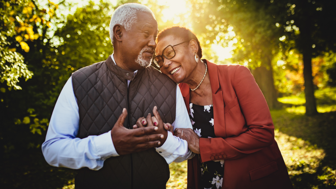Smiling older couple embracing outdoors at sunset, symbolizing secure survivor planning and support.