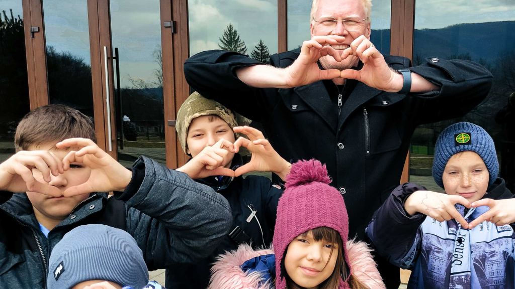 Michael Brady smiling with a group of Ukrainian children at Winter Camp Dreamland, all bundled in warm coats and hats, enjoying time together outdoors.